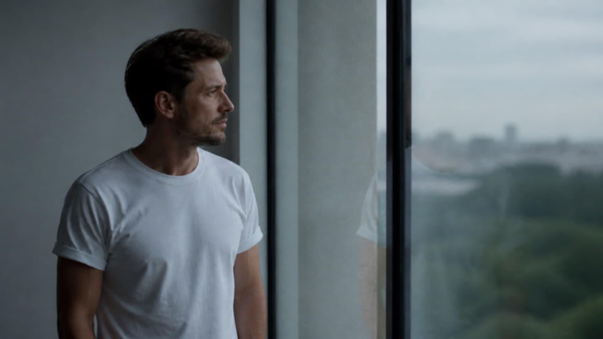 A man in a plain white T-shirt by a window